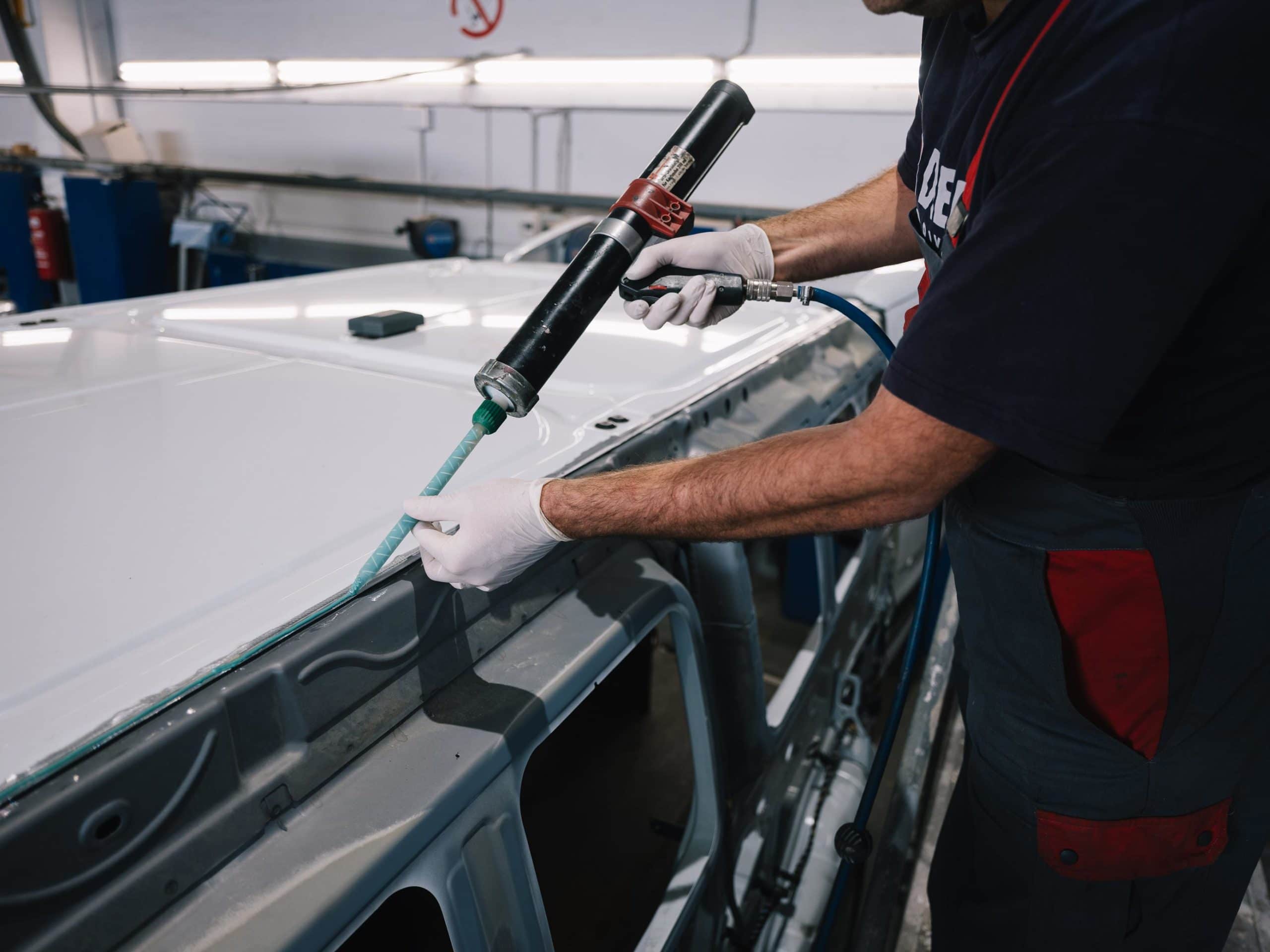Hände eines Werkstattmitarbeiters die eine Silikonspritze halten um Karosseriearbeiten zu verrichten